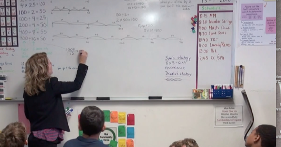 Female teacher standing at a whiteboard. Students are sitting in front of her. Math equations on the board.